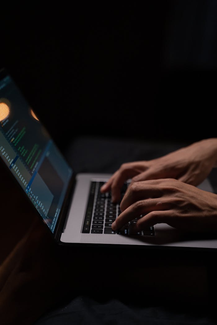 Services-03 Hands typing code on a laptop keyboard in a dark room, capturing the essence of late-night programming.