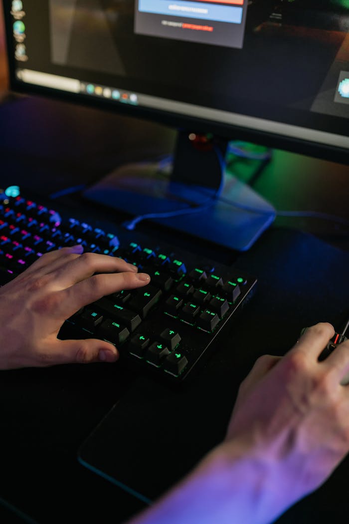 mobile-02 Close-up of hands using a keyboard and mouse on a gaming setup with colorful lights.