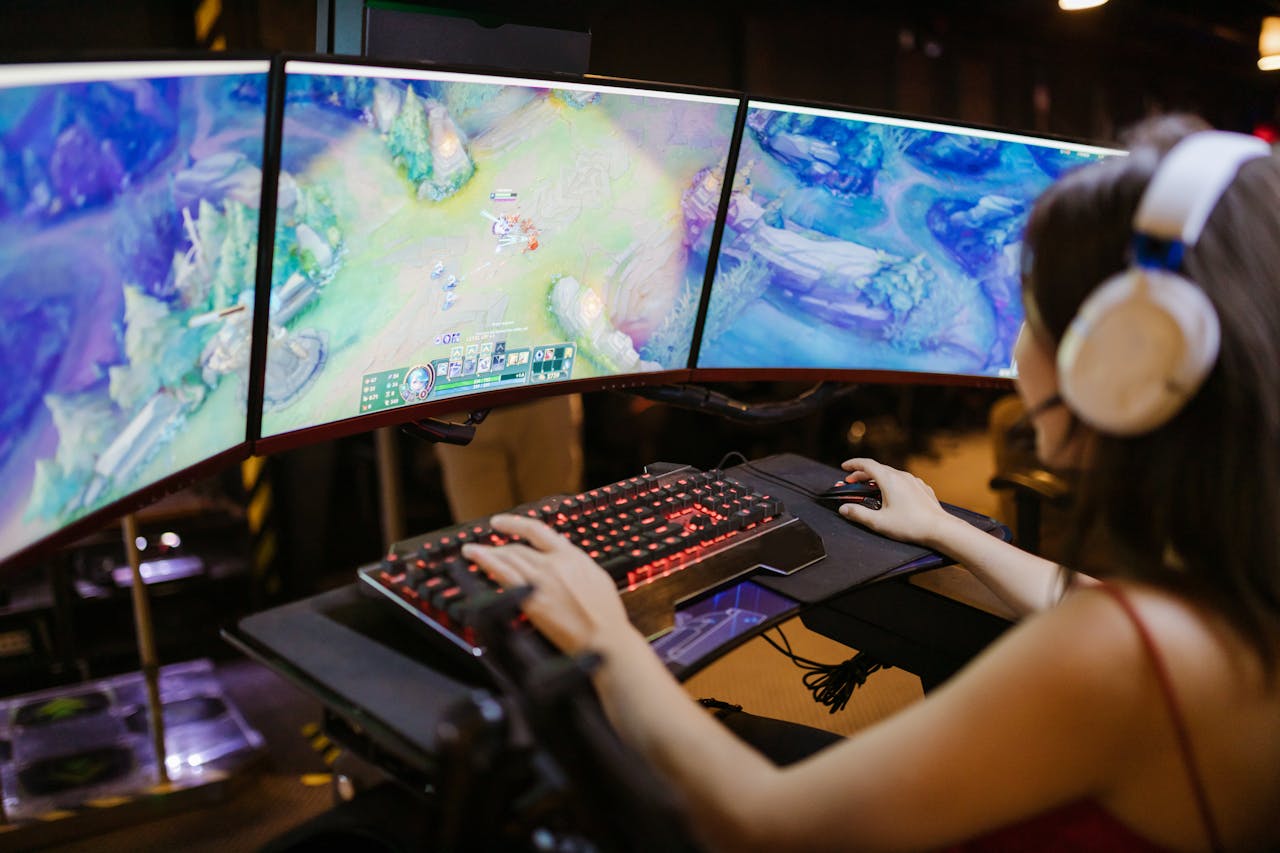 creative-02 A young woman intently gaming on a multi-screen setup, showcasing vibrant gaming visuals.
